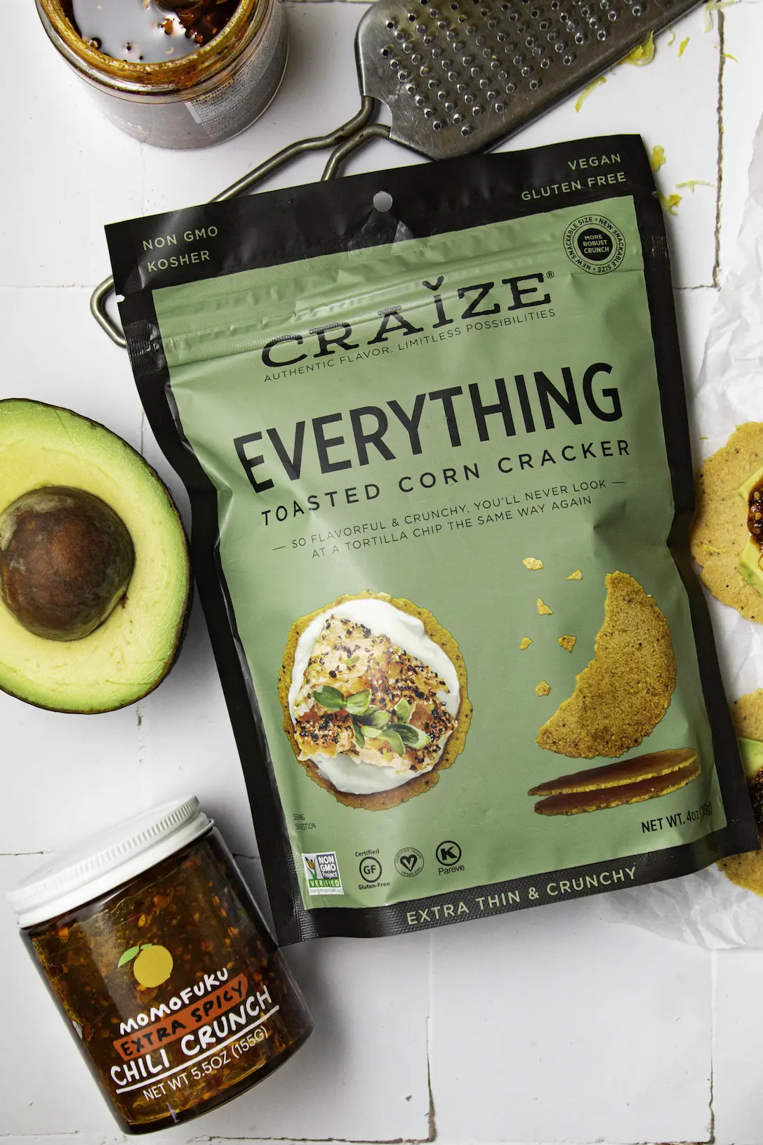 Craize Everything toasted corn cracker bag with avocado half and chilli crunch jar nearby.