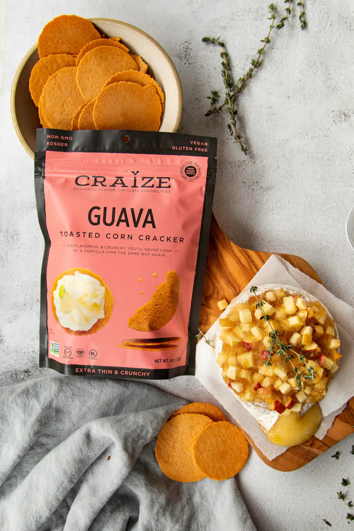 Craize Guava crackers bag with a board of crackers and a round cheese topped with diced apples.
