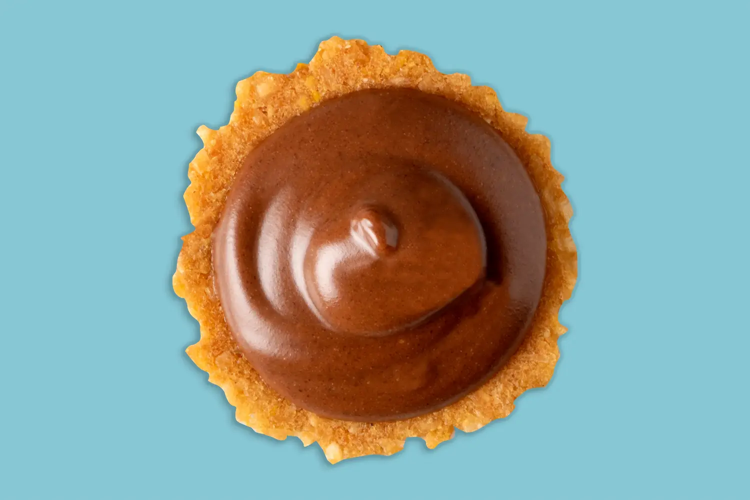 Close-up of glossy chocolate spread on a round cracker against a blue background.