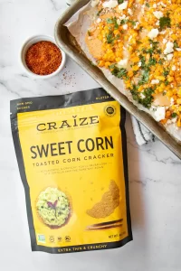 Craize Sweet Corn crackers bag next to a tray of loaded corn nachos with cheese and herbs.