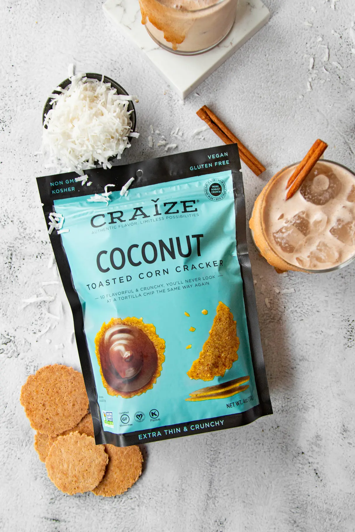Craize Coconut bag with iced drink, cinnamon sticks, shredded coconut, and crackers on grey surface.