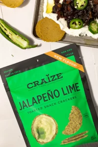 Craize Jalapeño Lime crackers bag beside dip topped with meat and sliced jalapeños.